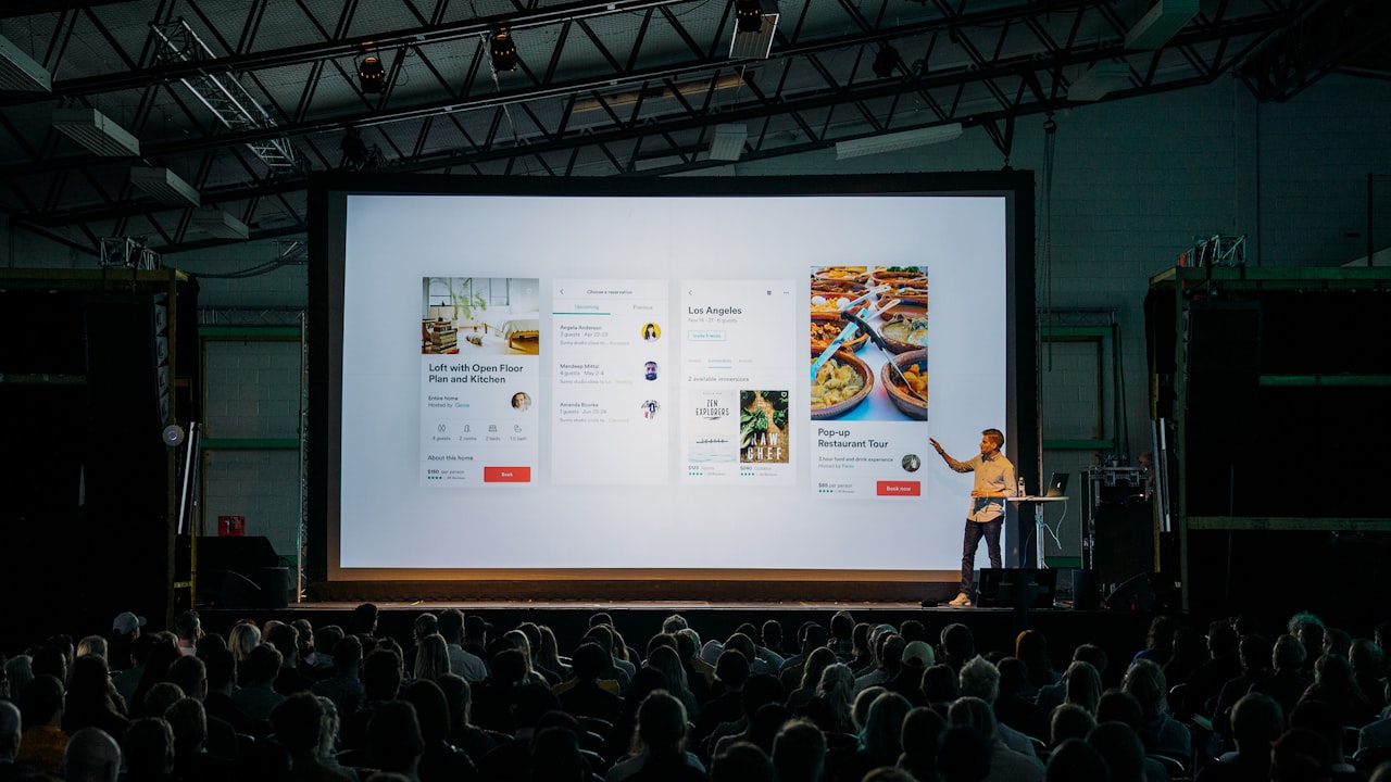 Speaker presenting on a large conference stage to a live audience